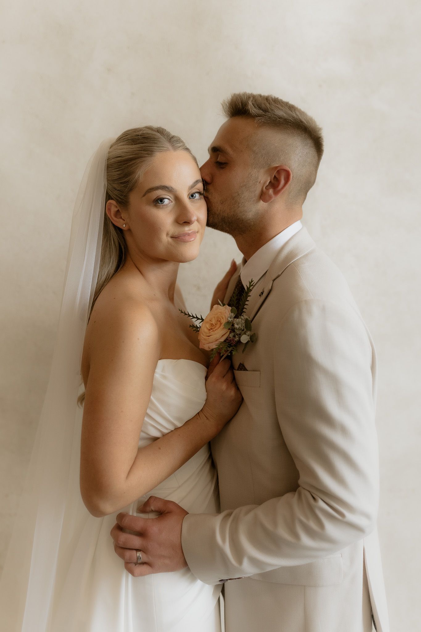 Intimate portrait of couple in romantic wedding moment against neutral background.