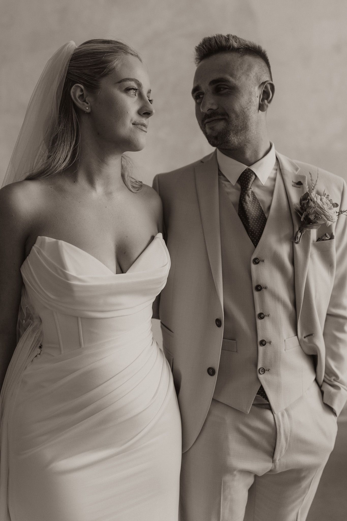 Elegant couple in wedding attire, with bride in white dress and groom in light colored three-piece suit.