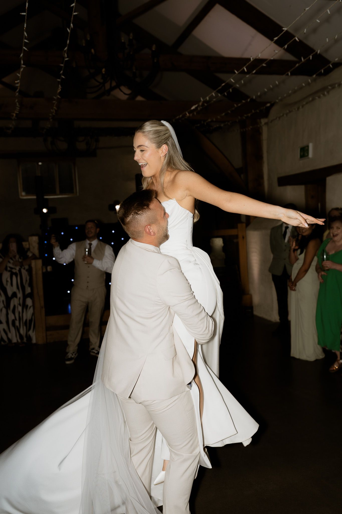 A joyful first dance moment at a wedding reception with the groom lifting the bride in her flowing white gown.