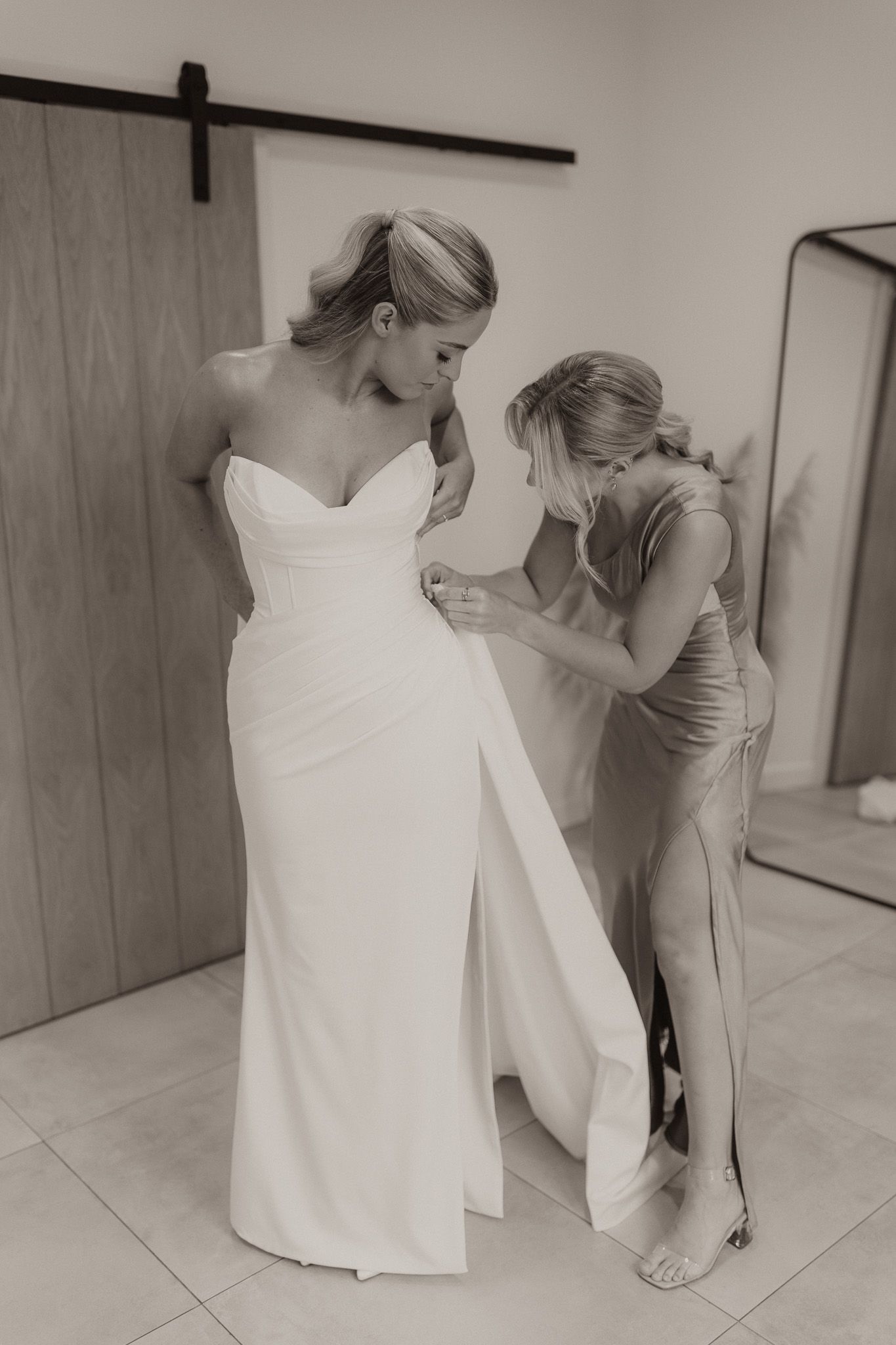 A wedding dress fitting where final adjustments are being made to an elegant white strapless gown.