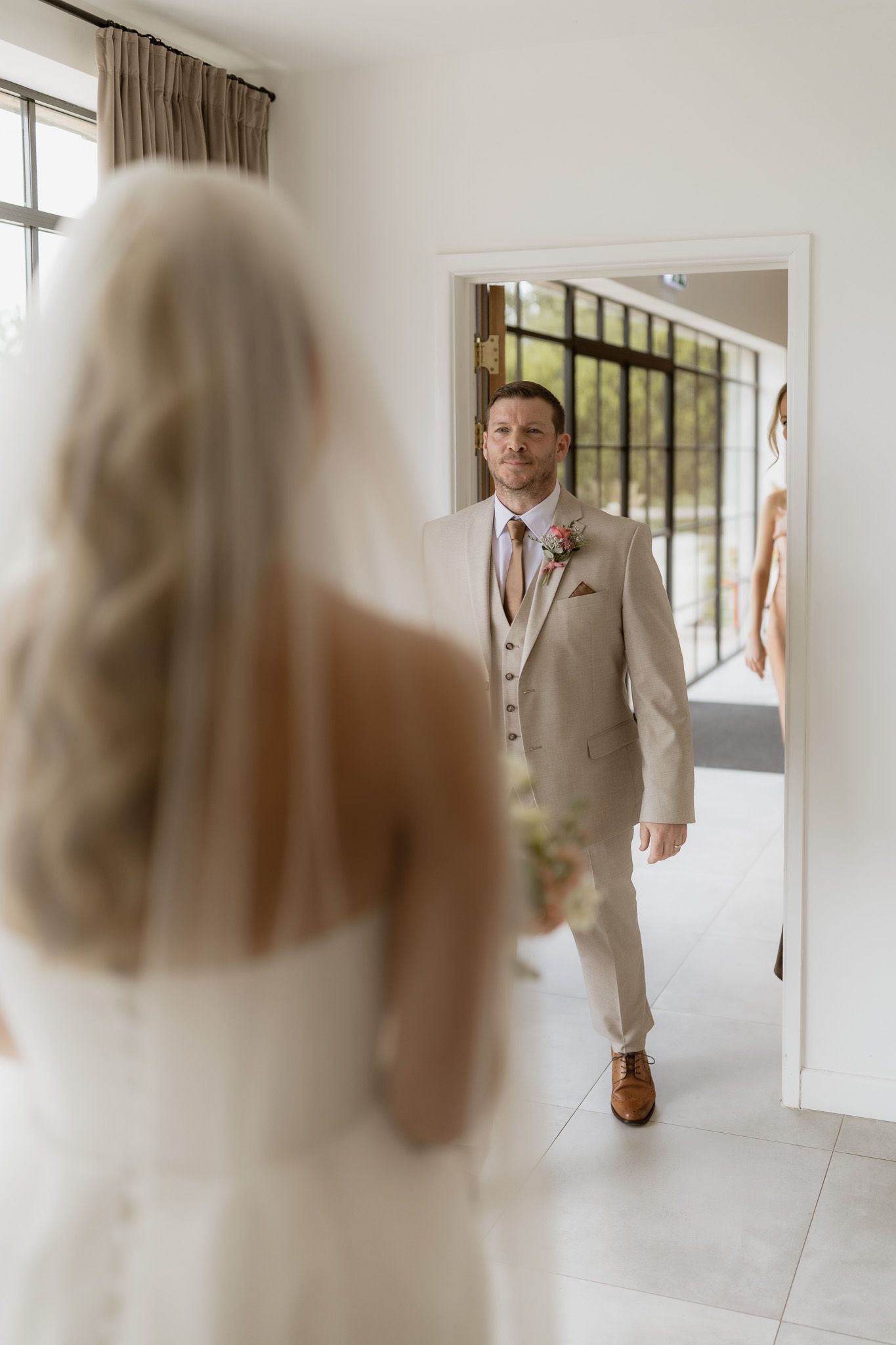 A first look wedding moment showing the groom in a tan suit seeing the bride in her white dress and veil for the first time.