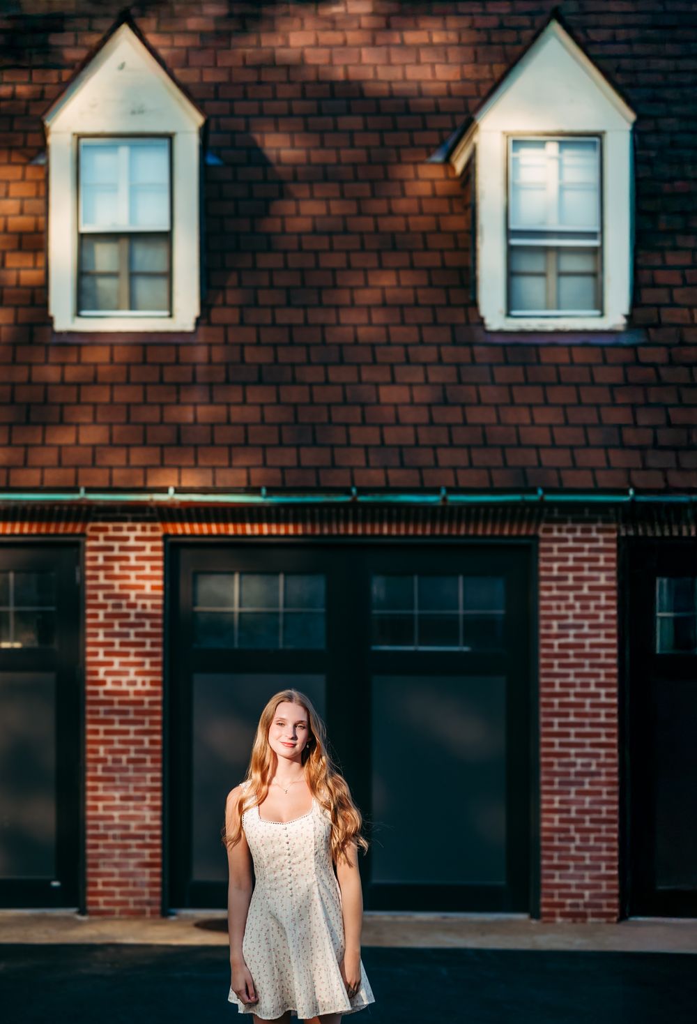 Sunlit white summer dress against a classic brick building with dormer windows.