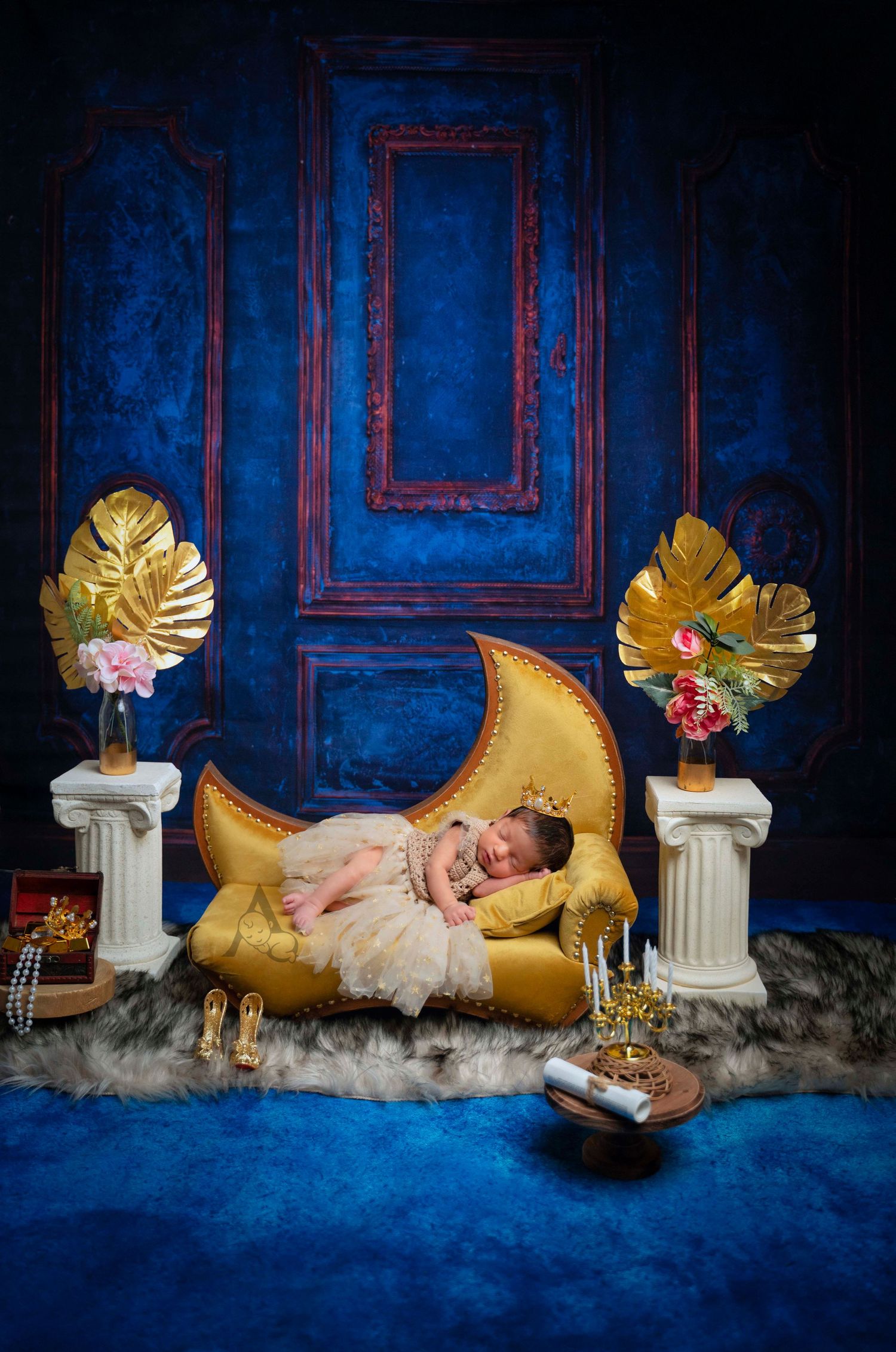 Newborn photography setup with golden moon prop against deep blue walls with decorative gold accents.