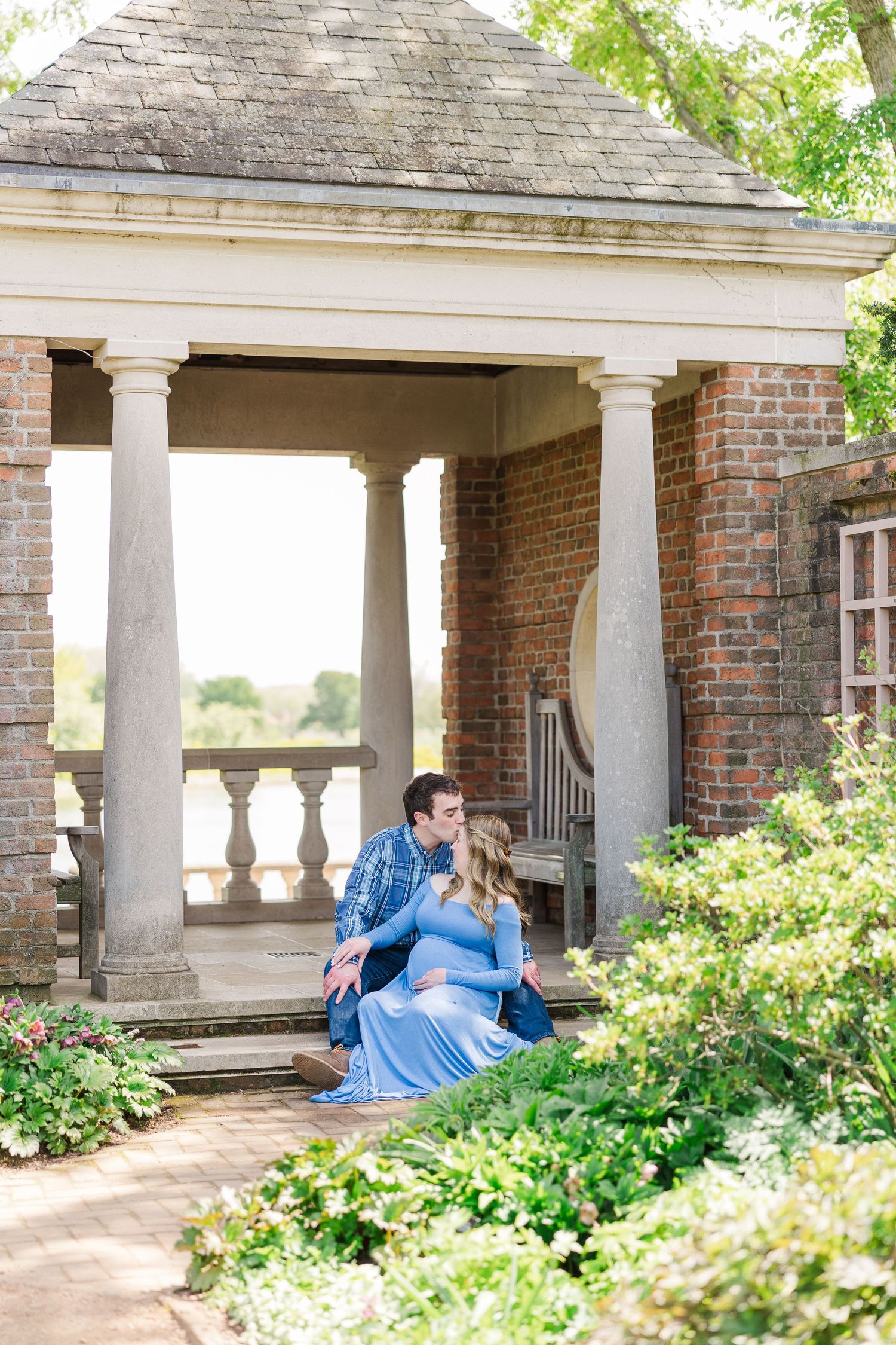 Couple sits together on brick porch steps with white columns and lush greenery at historic estate. at Chicago Botanic Garden