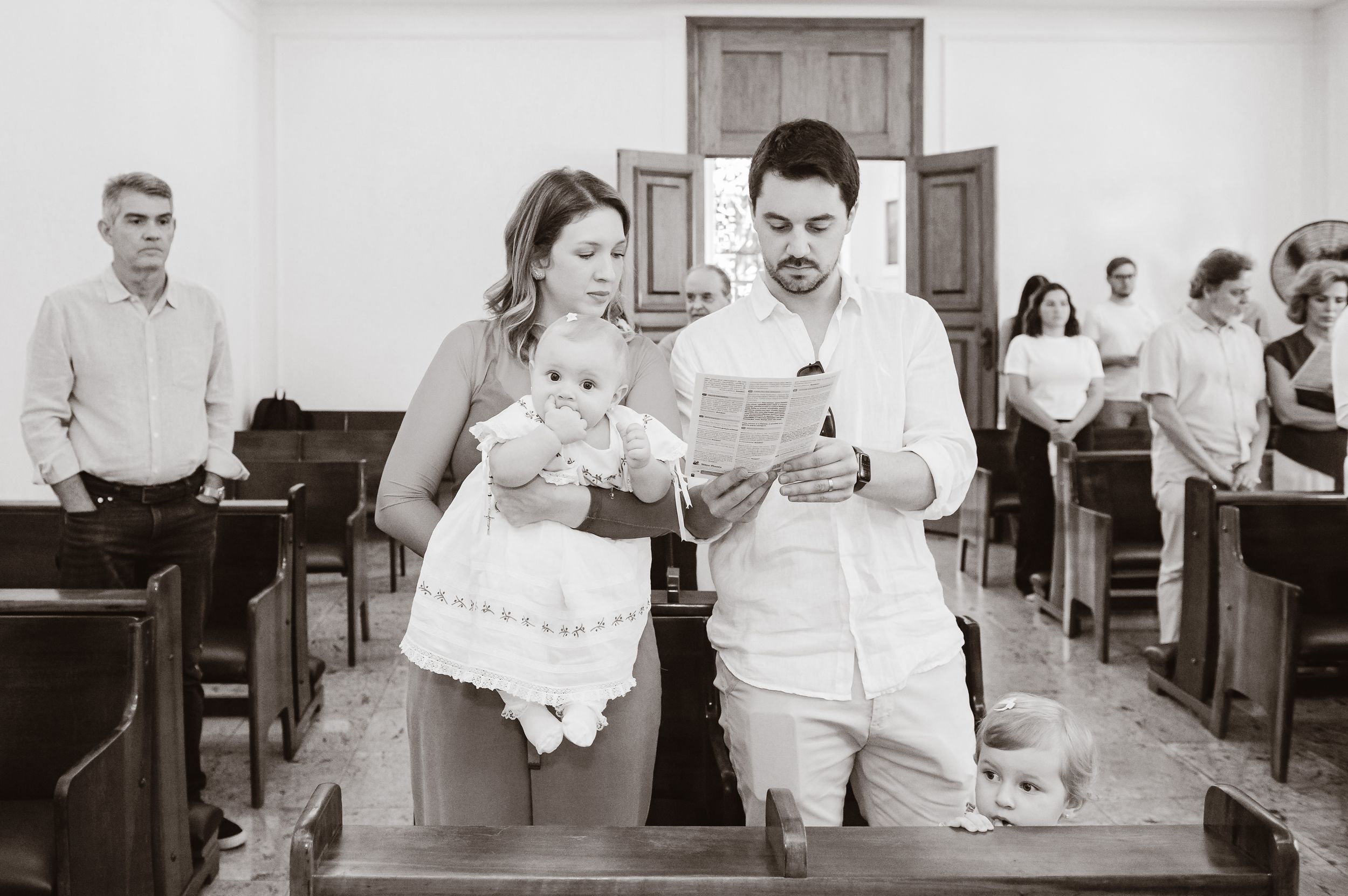 A couple in white attire walk down the church aisle together during a ceremony while other guests watch from the pews.