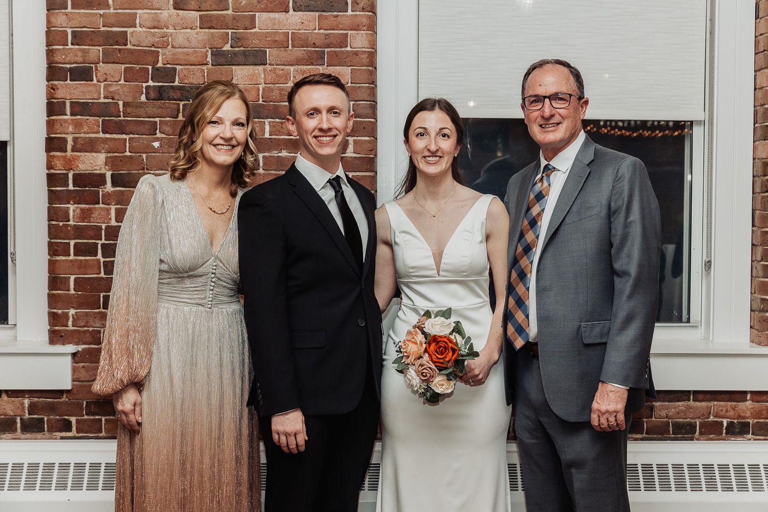 Group in formal attire poses together at small wedding gathering in front of brick building exterior.