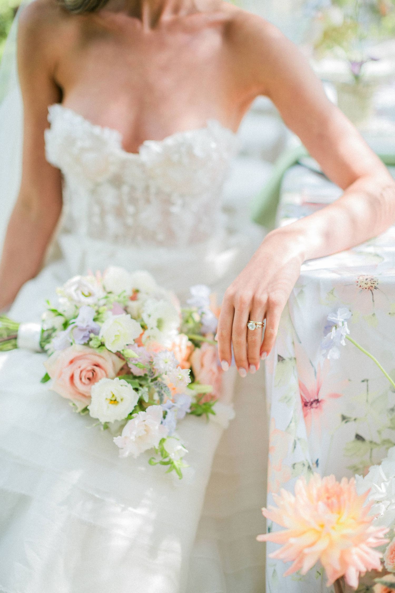 A white bridal gown shown with a delicate peach, lilac and white floral bouquet and ring detail and floral linens. Euridge wedding Hayley El