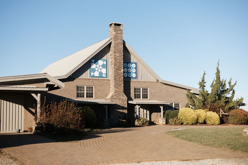 A modern mountain lodge with stone chimney and tan exterior features a circular driveway and rustic architecture.