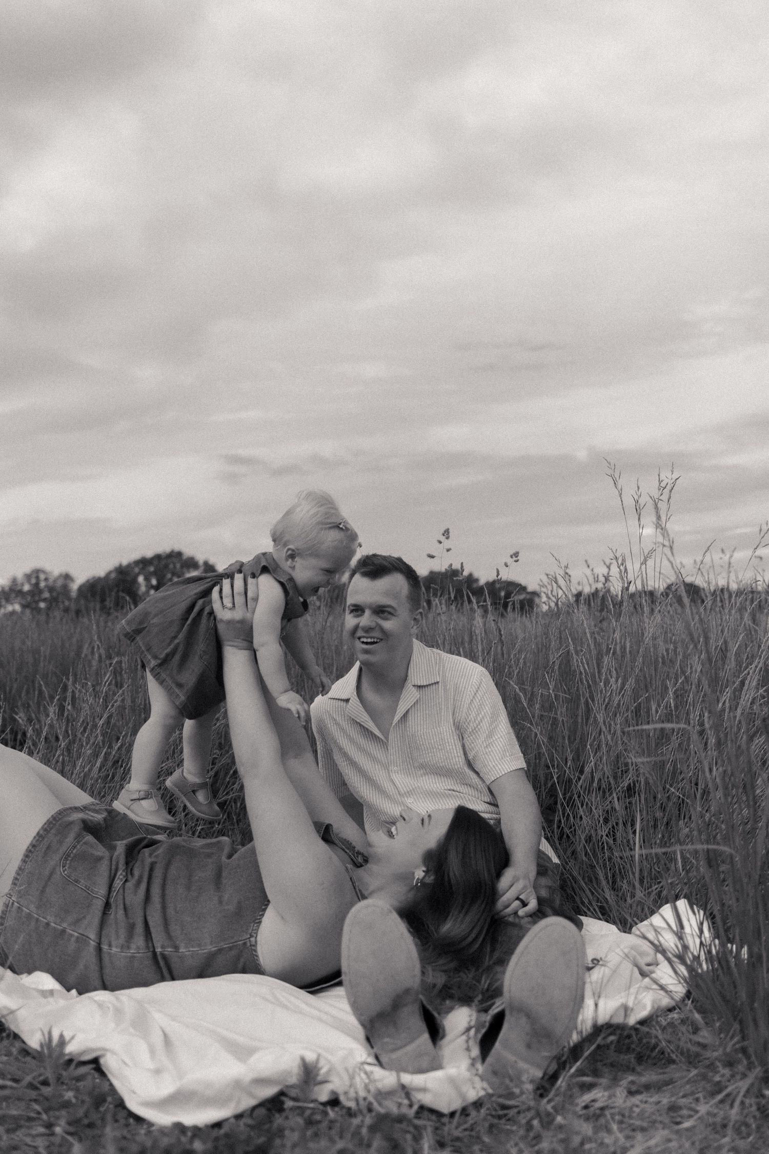 Vintage black and white photo of a family relaxing on a blanket in a grassy field.