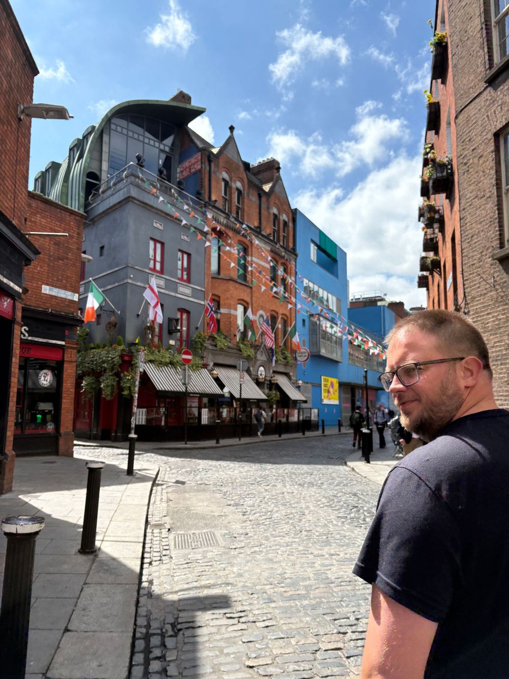 Historic brick buildings and cobblestone street in Temple Bar district of Dublin with Irish flags and sunny blue sky.
