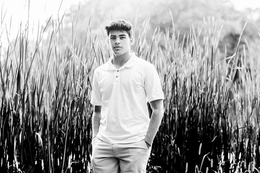 Black and white portrait of a person in a white polo shirt standing in front of tall grass.