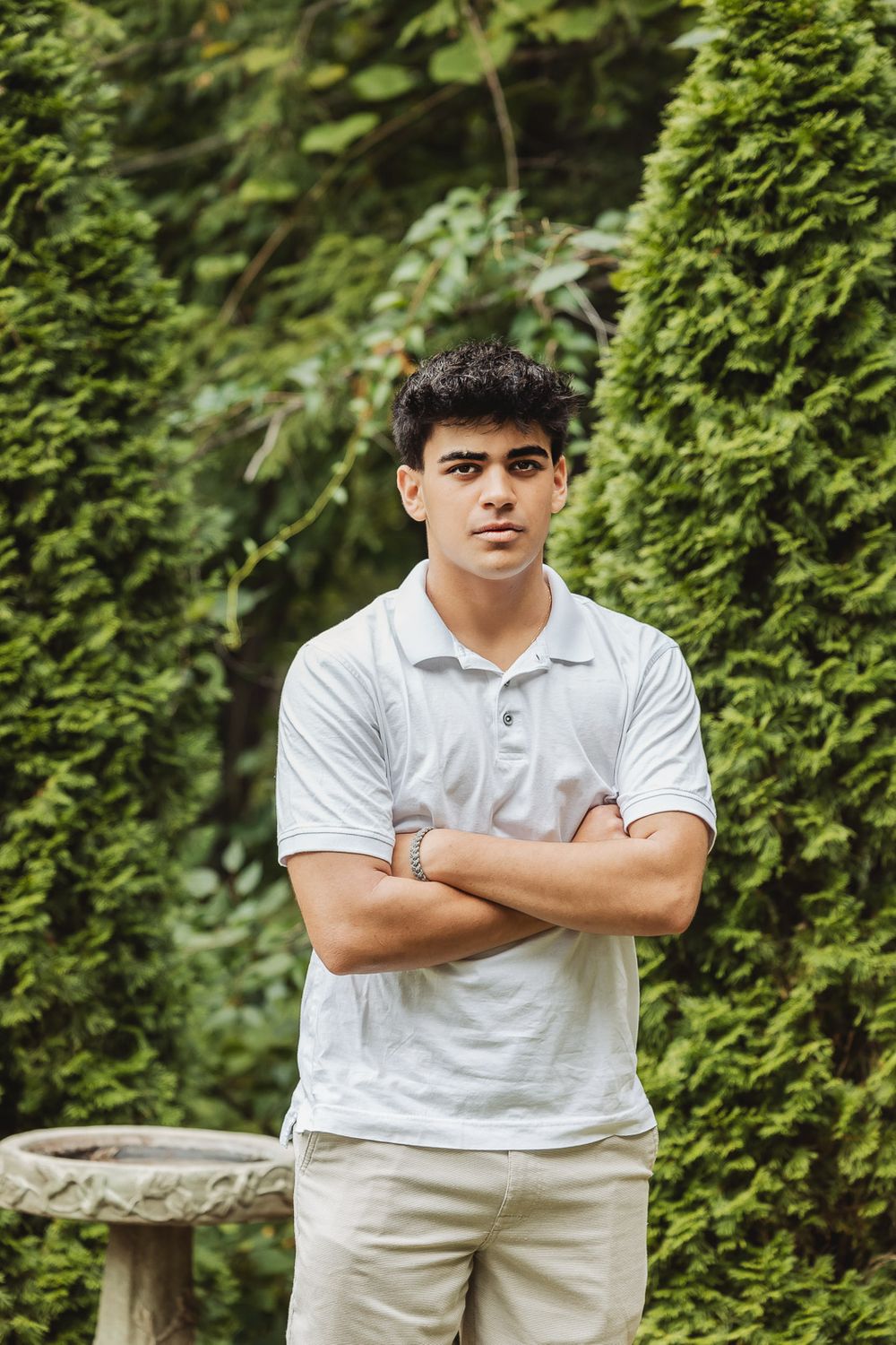 Four sequential photos of someone wearing a white polo shirt and khaki pants posing against green bushes outdoors.