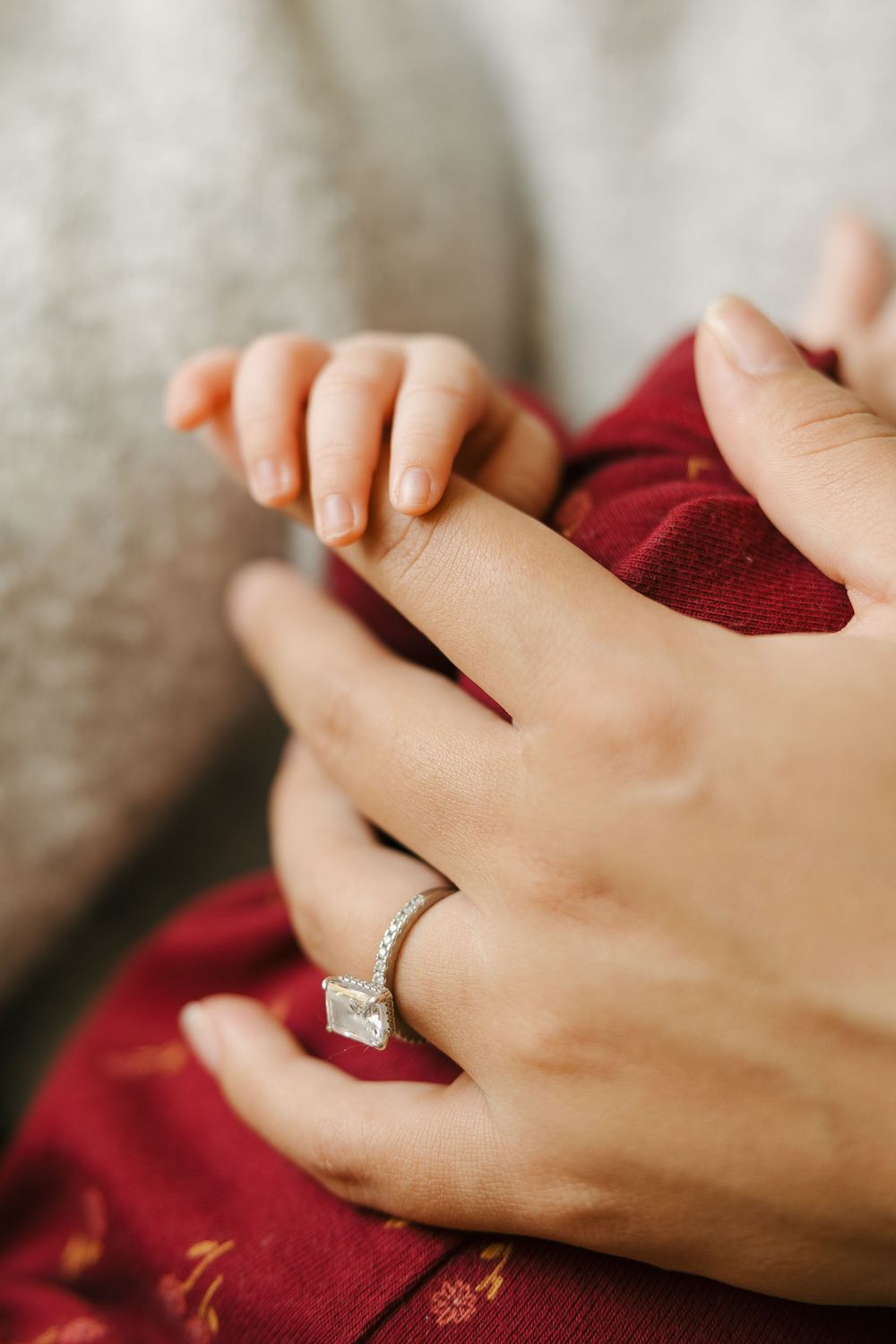 Close-up photo of hands wearing a diamond engagement ring against a burgundy red fabric background.