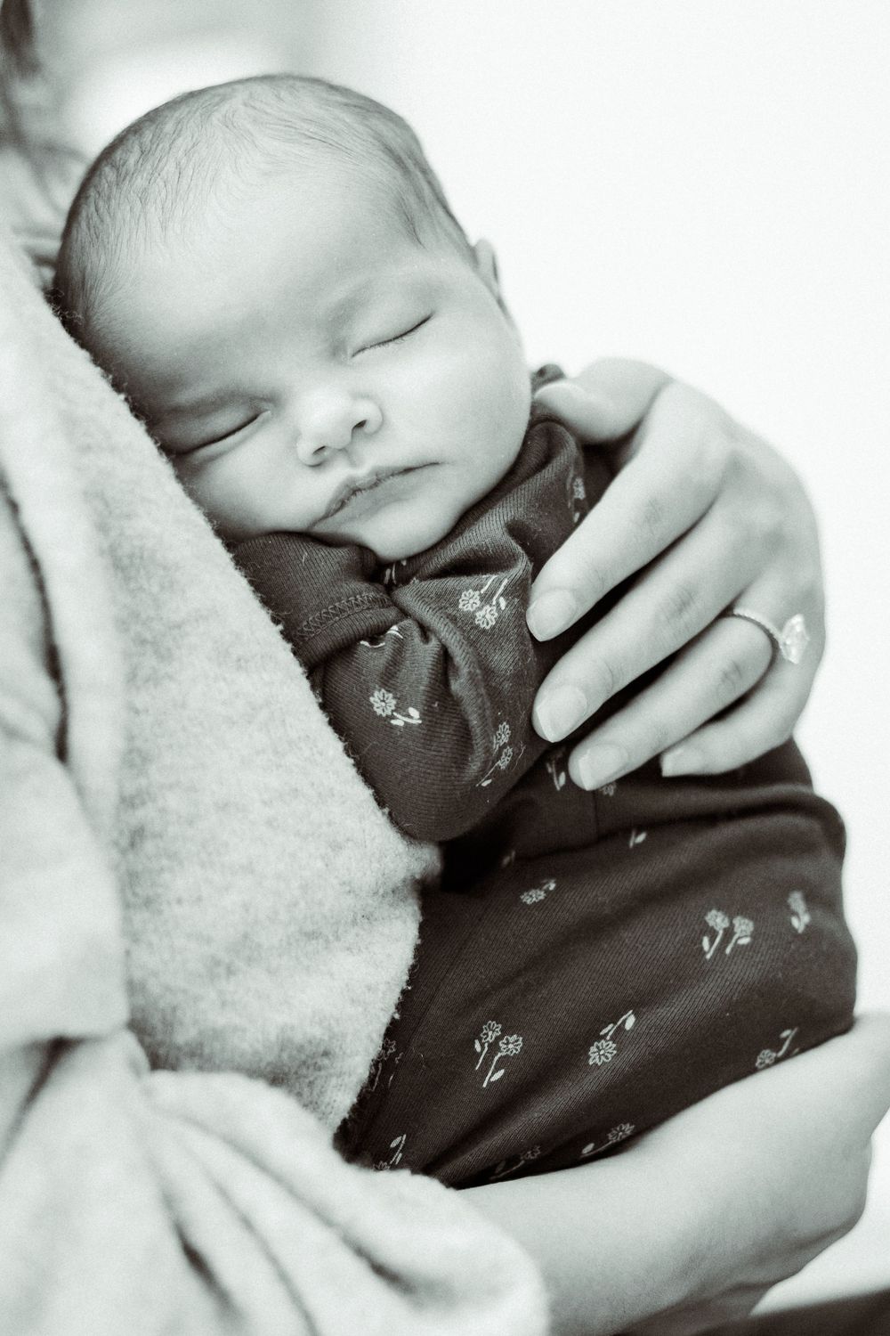 A peaceful sleeping newborn baby wrapped in a blanket with floral pattern clothing in black and white photography.