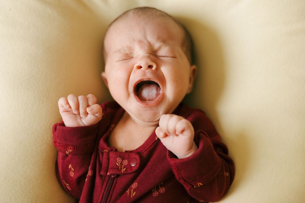 A series of candid baby expressions showing yawning, laughter, and smiles against a soft beige background.