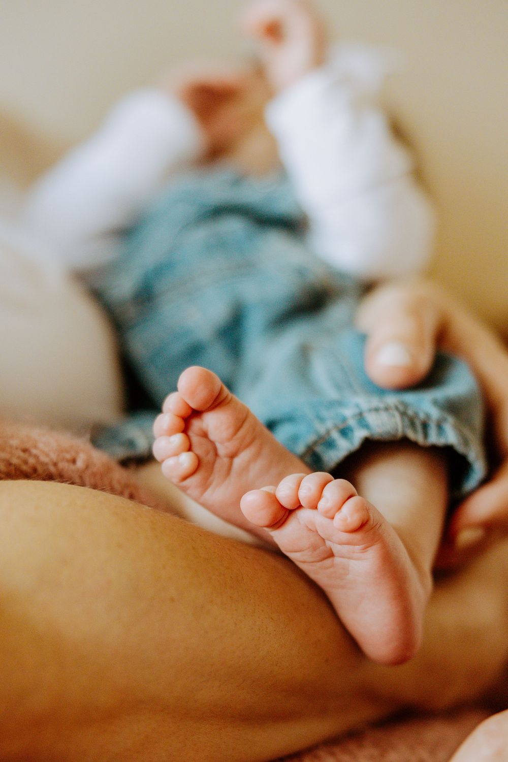 Close-up photo of tiny baby feet against soft turquoise fabric with shallow depth of field creating a warm, intimate mood.