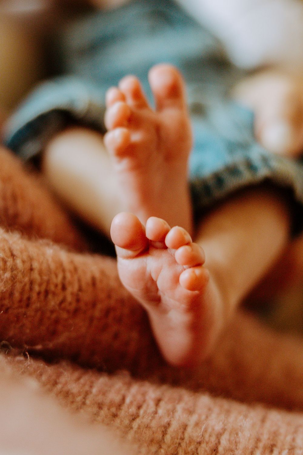 Macro shot of tiny baby toes resting on a brown knitted blanket in warm lighting.
