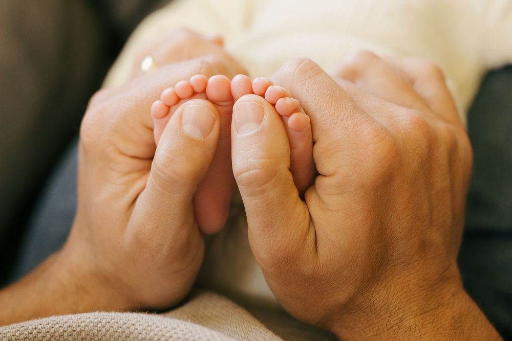 Adult's hands gently holding tiny baby feet in a tender moment, with soft natural lighting.