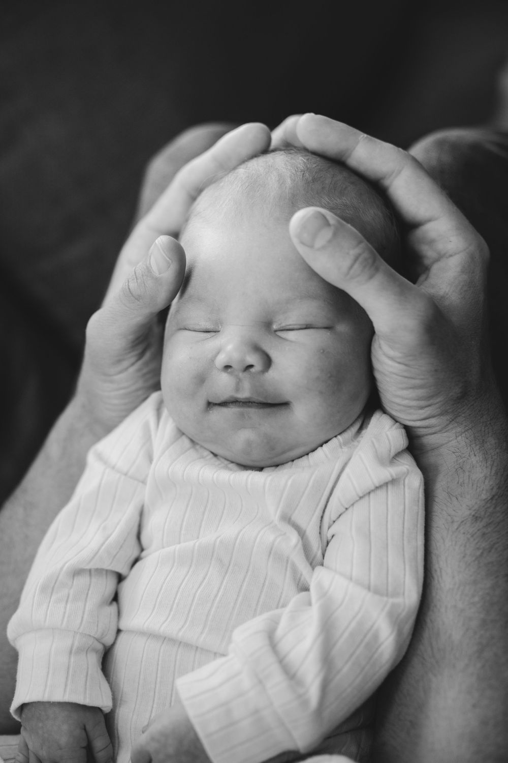 Black and white image of a peaceful sleeping newborn baby cradled in adult hands wearing a ribbed sweater.