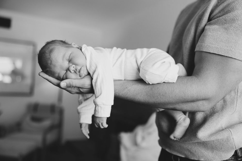 An array of black and white photographs showing hands holding and comforting a baby in various tender moments.