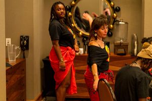 Dancers performing in traditional African clothing with gold curtains and string lights in the background.