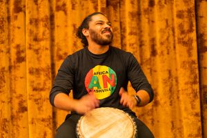 Drummer wearing African Unity shirt performs enthusiastically on djembe drum.