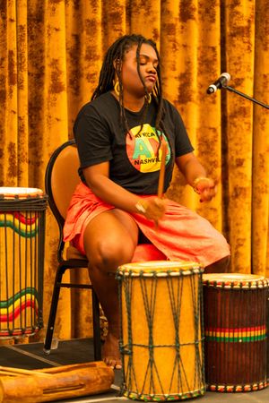 Musician playing vibrant African drums with orange curtain backdrop during cultural performance.