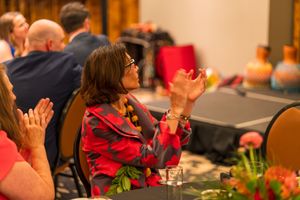 Audience member in red floral dress clapping during performance.