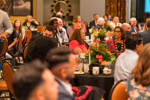Diverse audience enjoys performance at formal dinner event with floral centerpieces.