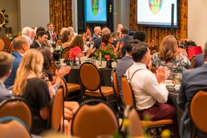 Conference attendees seated in rows at round tables in an elegant ballroom setting.
