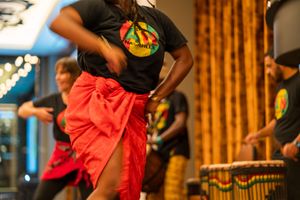 Performer in a black t-shirt and red wrap skirt dancing during a cultural performance.