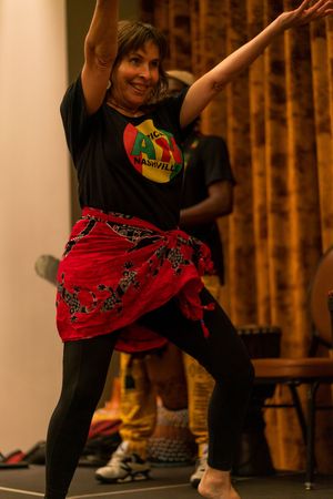 Dancer in black clothing and red skirt performs expressive movements in warm-lit studio.