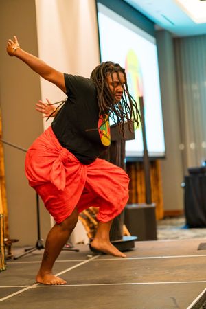 Performer executes graceful dance move in red and black attire on stage with warm lighting.
