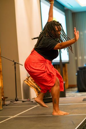 Dynamic dancer in red performs expressive movements across a studio floor during a contemporary dance sequence.