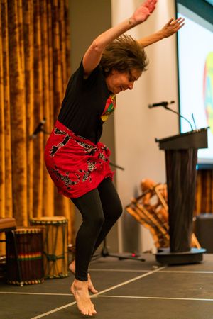 Performer in black top and red skirt dances barefoot during artistic performance on stage.
