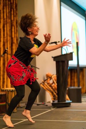 A dancer in black pants and red top performs a dynamic leaping movement sequence on a wooden floor.