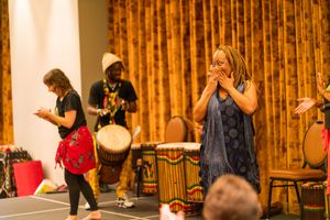 Performers playing drums and percussion instruments on stage with gold curtains in the background.