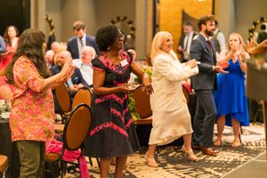 People in formal attire dance and celebrate during an indoor event with decorative lighting.