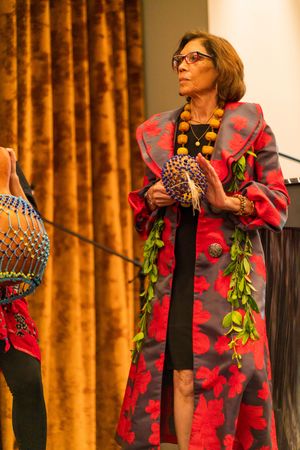 Performer wearing floral red dress and lei performs with traditional instrument on stage.