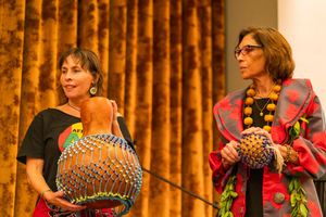 Two performers holding colorful musical gourds on stage with orange curtains.