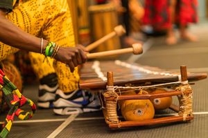 Musician playing a traditional wooden balafon instrument while wearing vibrant yellow attire and bracelets.