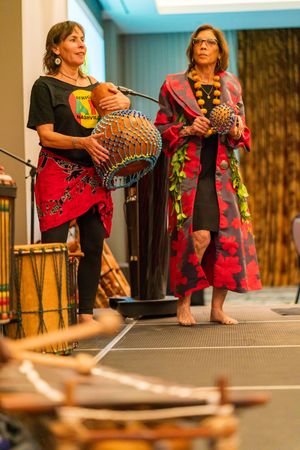 Two women performing with decorated percussion instruments on a stage.