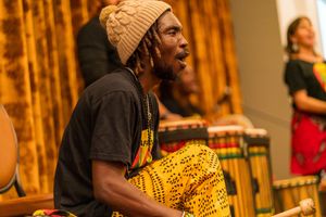 Performer in beanie hat playing traditional African instruments during indoor concert.