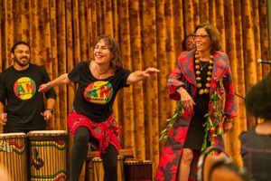 Performers in vibrant red and black outfits dancing during a cultural celebration with golden curtains.