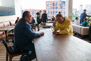 Two people engage in conversation while seated at a wooden table in a modern cafe setting.