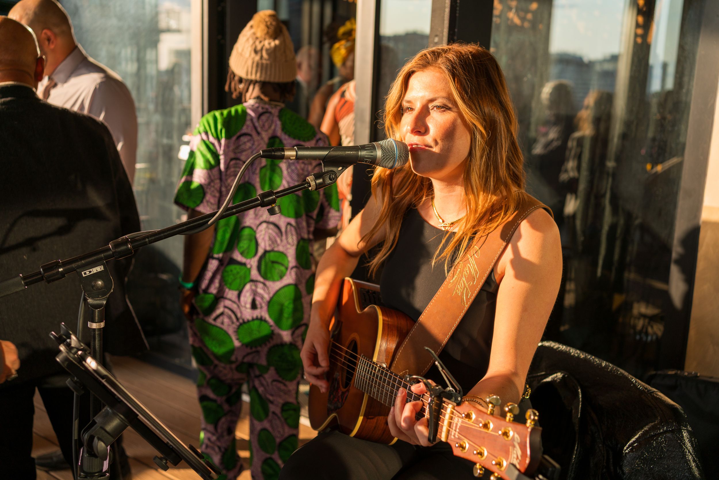 A performer sings and plays acoustic guitar at an intimate venue with string lights in the background.
