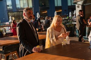 Two people stand at a bar counter at what appears to be a social gathering or event in an indoor venue.