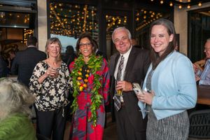 Group of people socializing at an evening event with decorative string lights in the background.