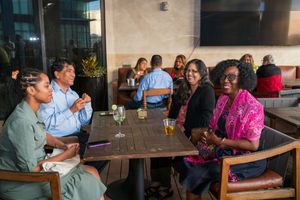 Diverse group of guests enjoying drinks and conversation at an outdoor patio restaurant table.