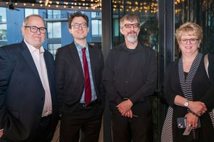 Group of four professionals pose together at formal event with string lights in background.